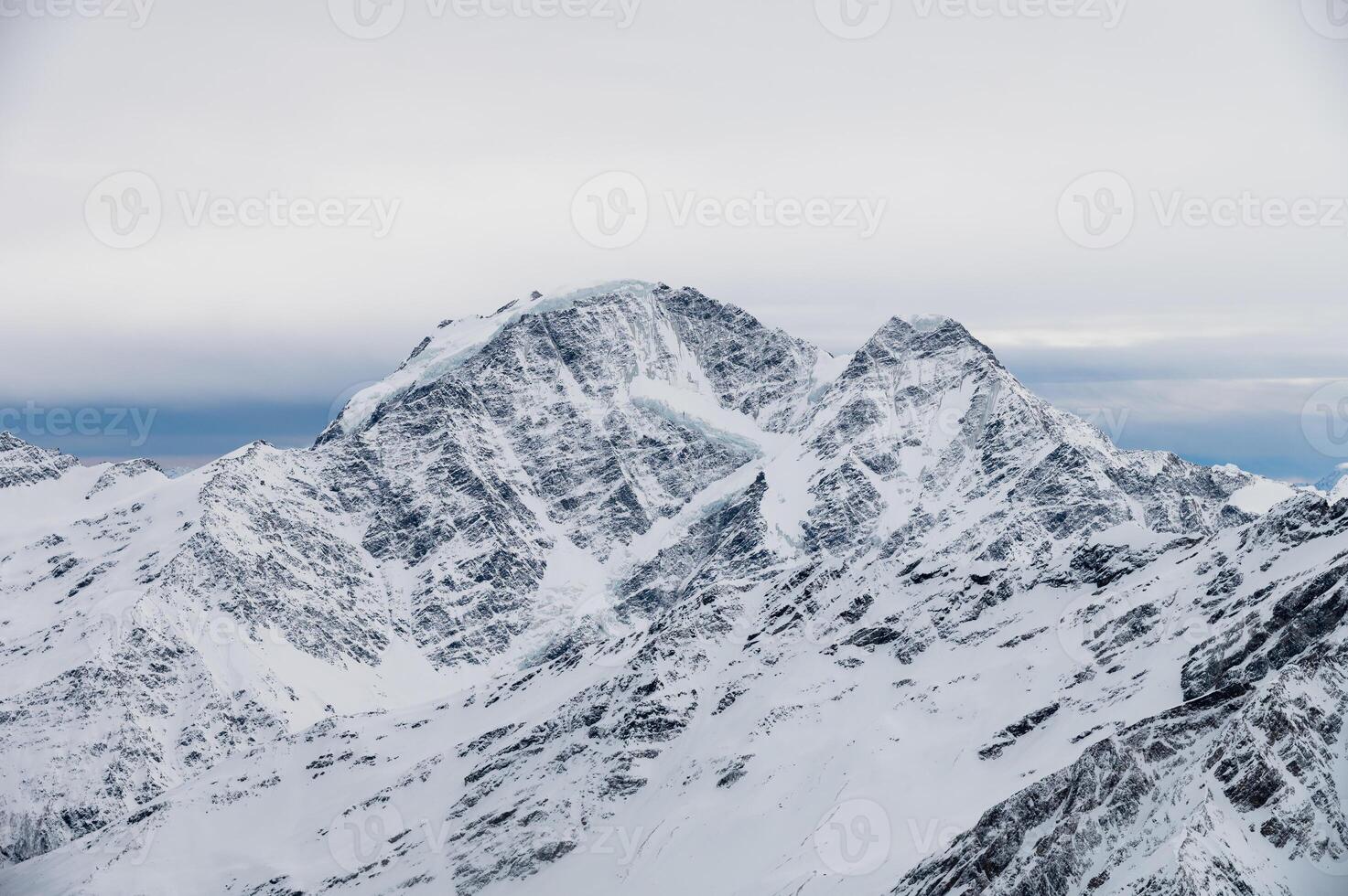 Picturesque view of mountain range with snow capped rocks under blue sky with white big cloud hanging over it in winter season photo