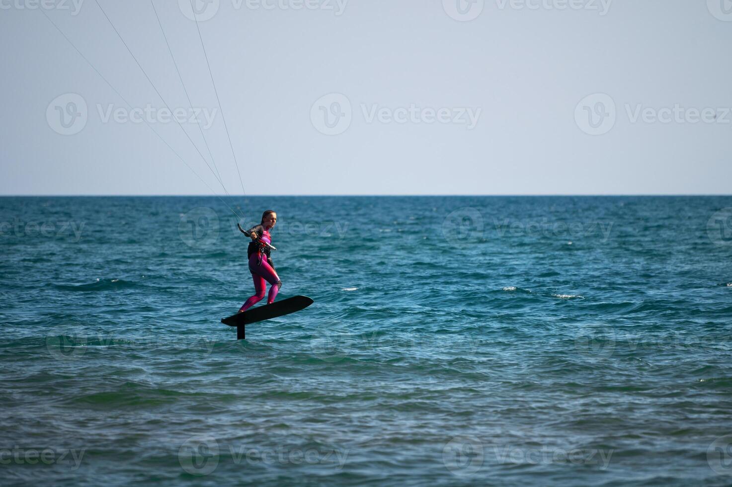 woman at sea rides a hydrofoil surfboard using a kite wing. Extreme sport, fast travel across the sea on a board photo