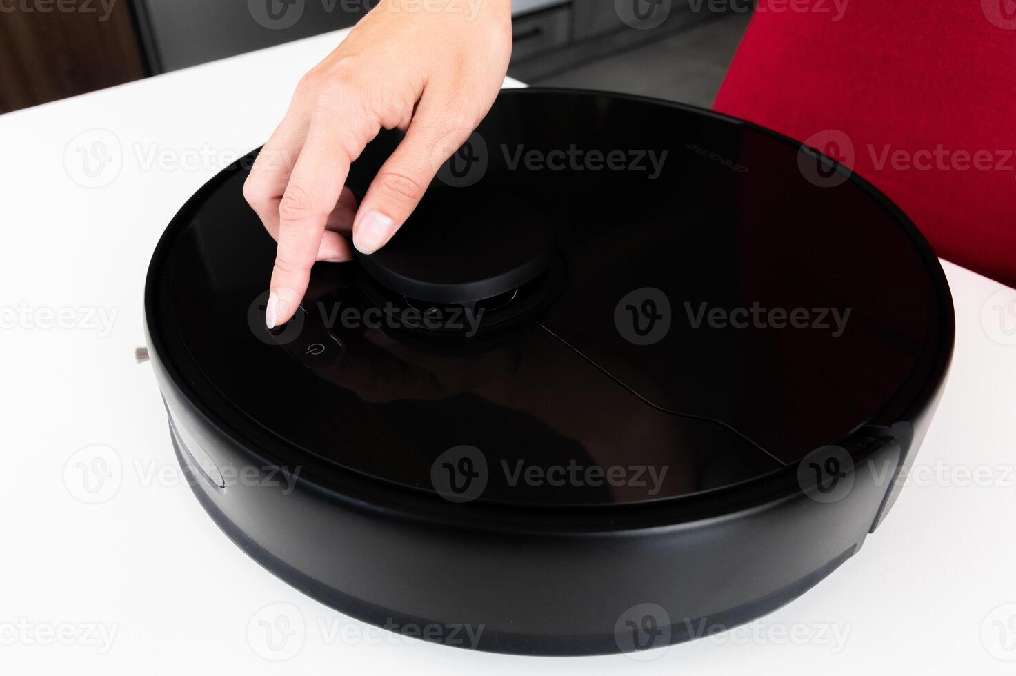 Robot vacuum cleaner with round black body on white background table, new home assistant, woman hand reaches out to turn it on and check, close-up photo