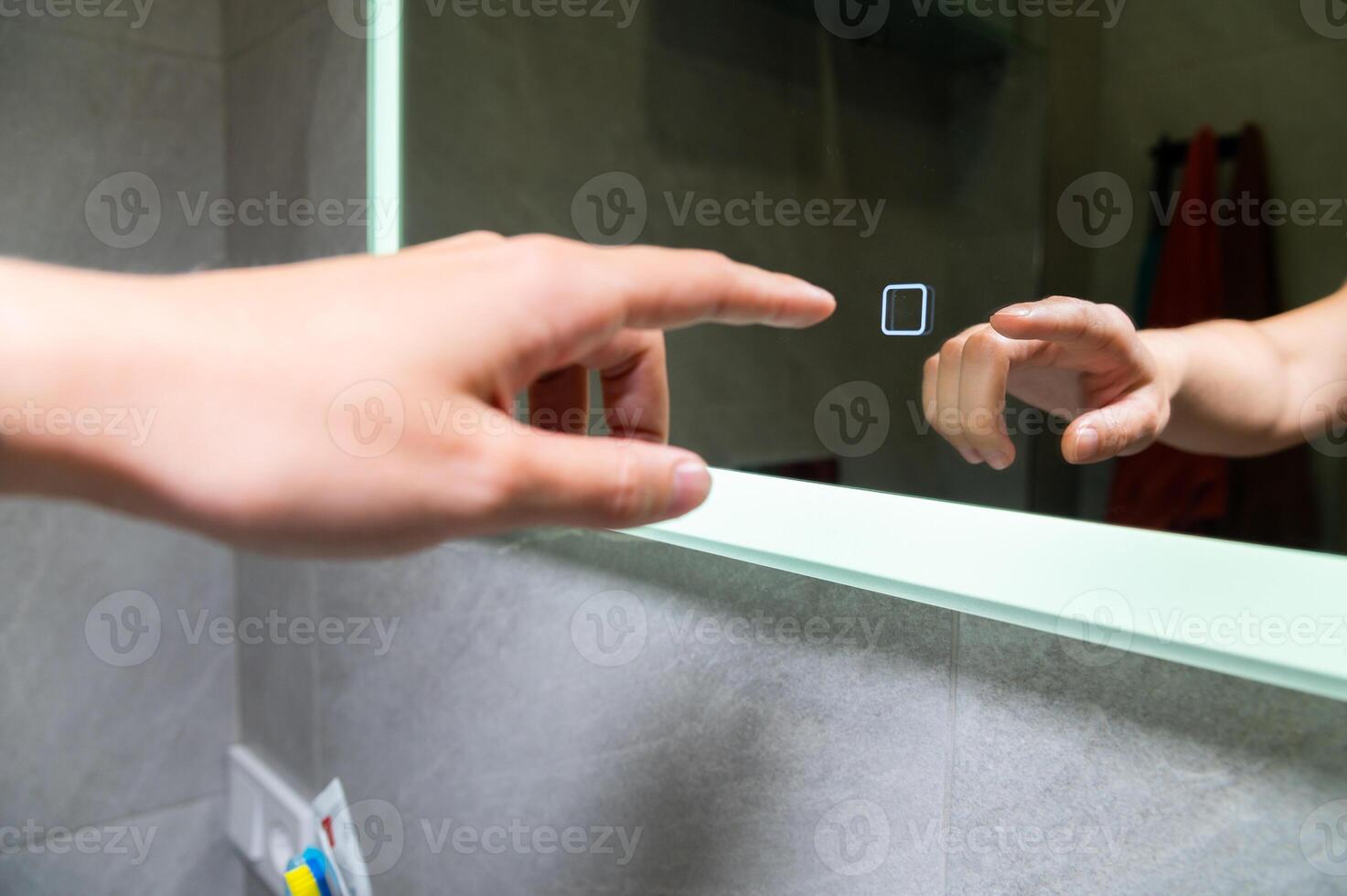 Woman's hand turns on the illumination of the bathroom mirror by touching the touch button on and off. Modern technologies photo