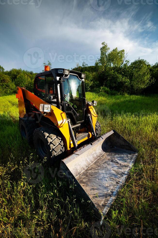 Small bulldozer will level the ground, preparing for new housing construction. Construction equipment on green grass in a field photo