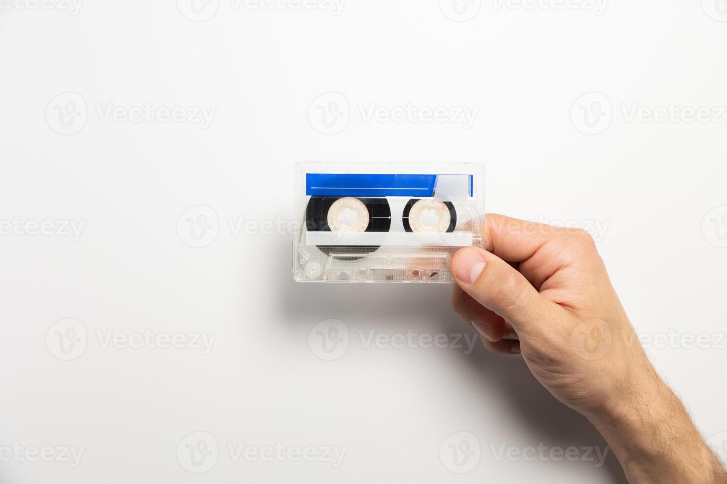 Close-up of a man's hand holding a blue cassette tape on a white background. Concept of music and sound, entertainment and nostalgia photo