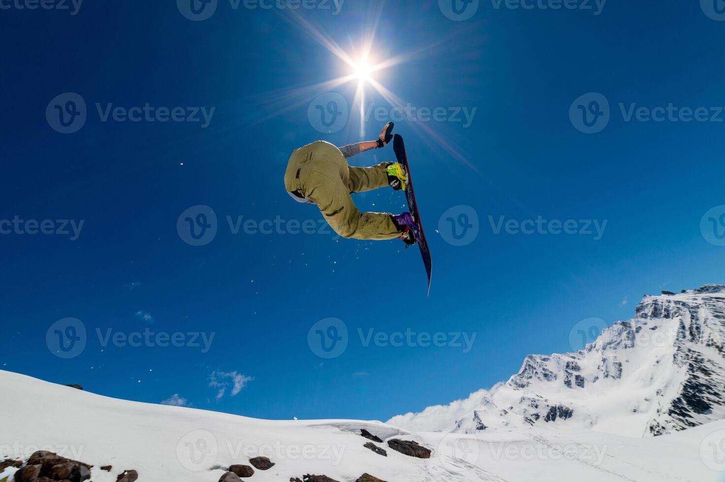 Jumping snowboarder on ski jump in alpine high mountains. Flying with ski jump on blue sky and bright sun photo