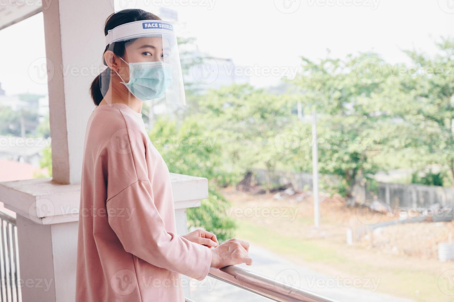 Asian woman wearing mask and face shield before going outside her room for prevent and protection covid-19 virus disease. Conceptual of new normal lifestyle after Covid-19 pandemic outbreak. photo
