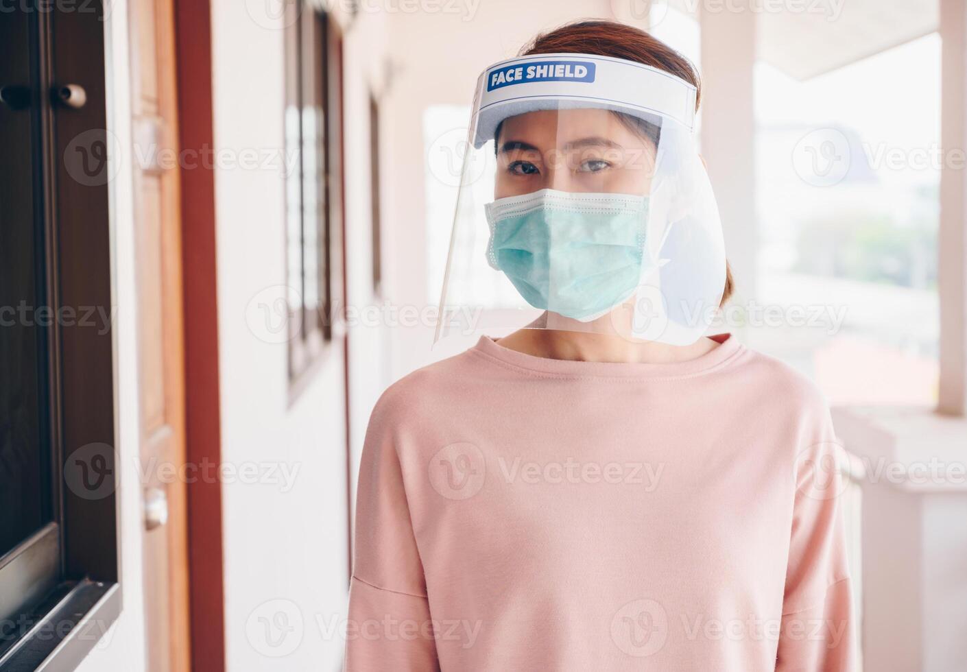 Asian woman wearing mask and face shield before going outside her room for prevent and protection covid-19 virus disease. Conceptual of new normal lifestyle after Covid-19 pandemic outbreak. photo
