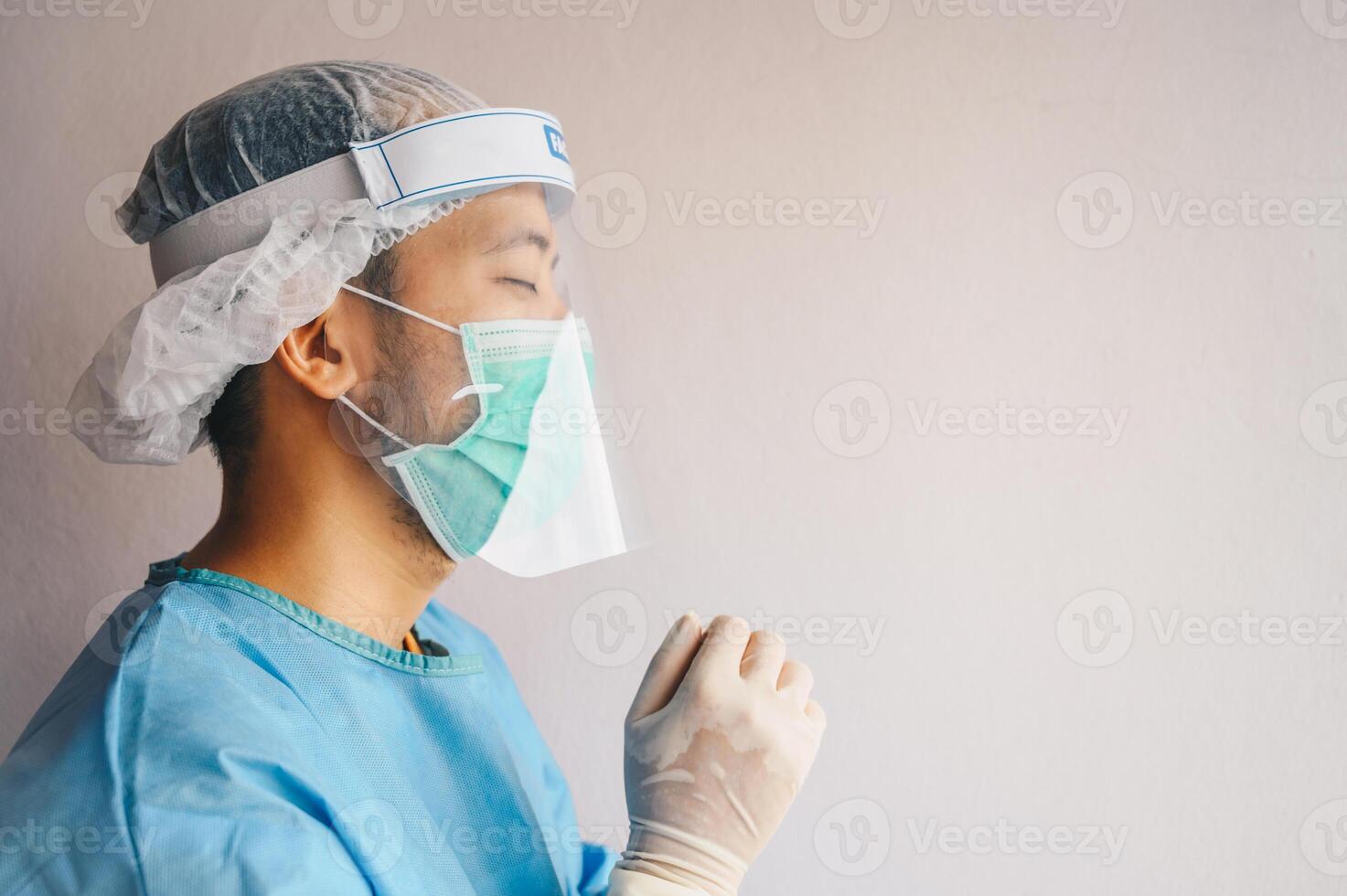 Portrait of Doctor praying for God's blessings while wearing PPE suit for work at hospital in covid-19 pandemic outbreak. photo