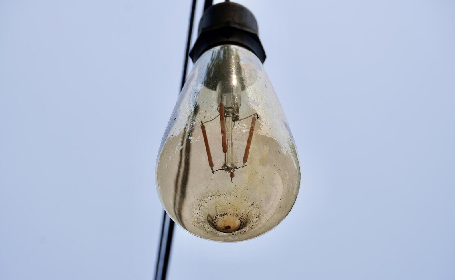 One single old hanging transparent light bulb isolated on horizontal outdoor plain sky environment background. photo