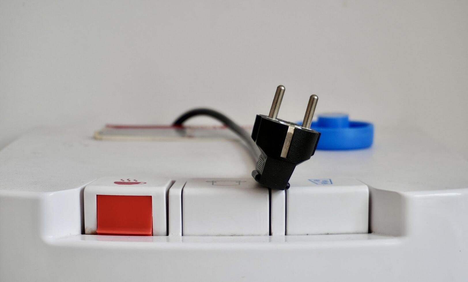 Black electricity plug on water dispenser surface and buttons isolated on horizontal indoor white wall background. photo