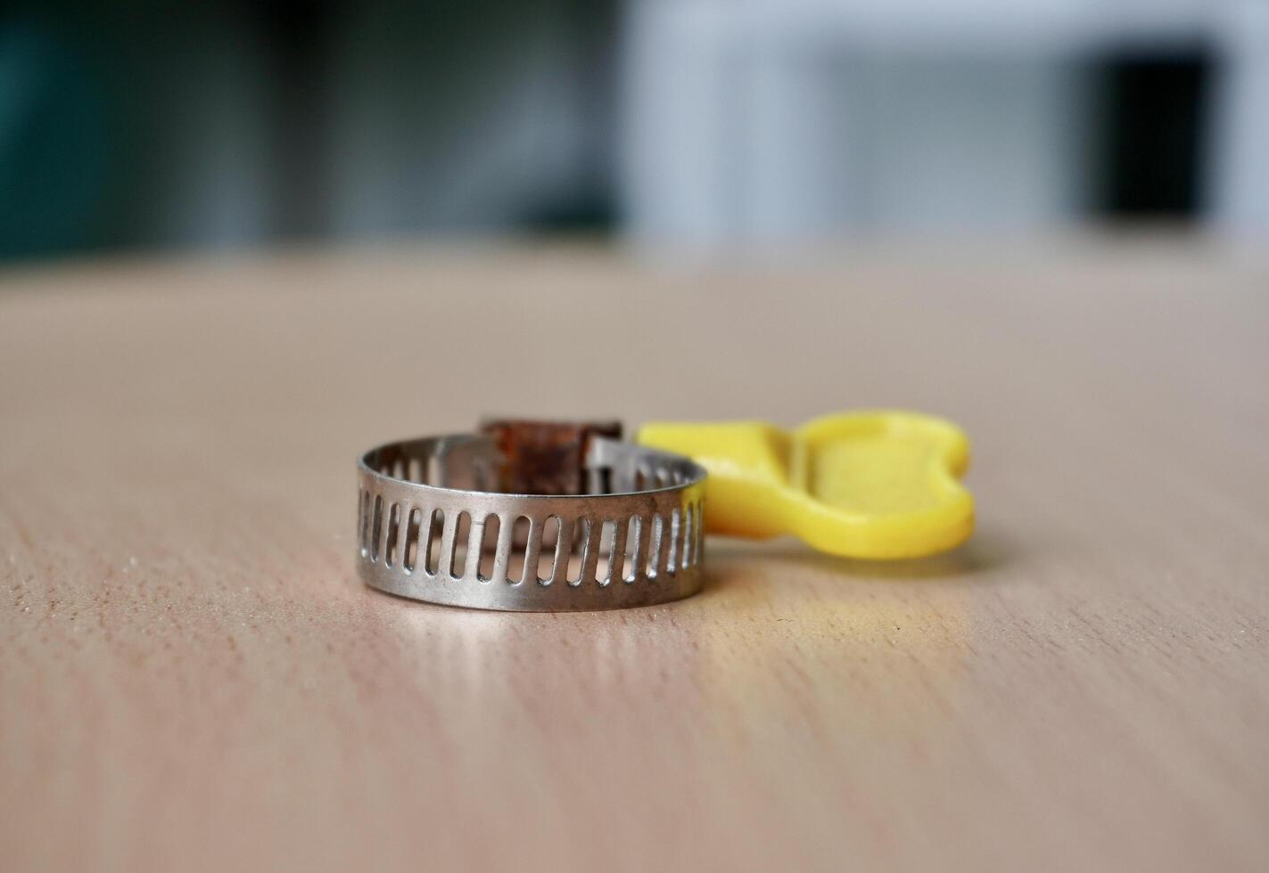 One small round metal hose clamp with yellow plastic fastener isolated on horizontal ratio wooden table surface background. photo