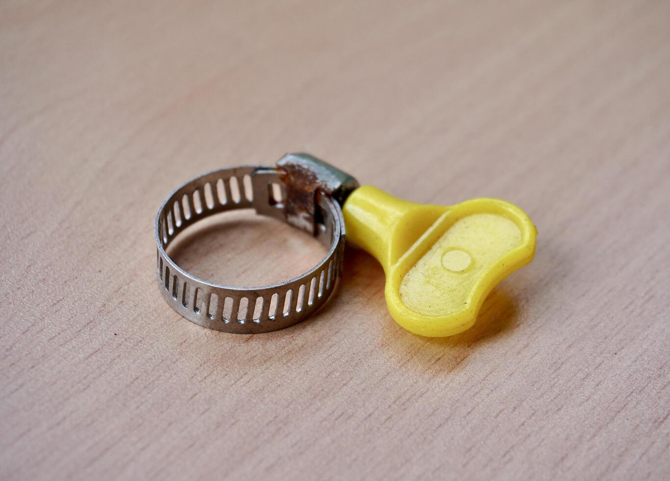 One small round metal hose clamp with yellow plastic fastener isolated on horizontal ratio wooden table surface background. photo