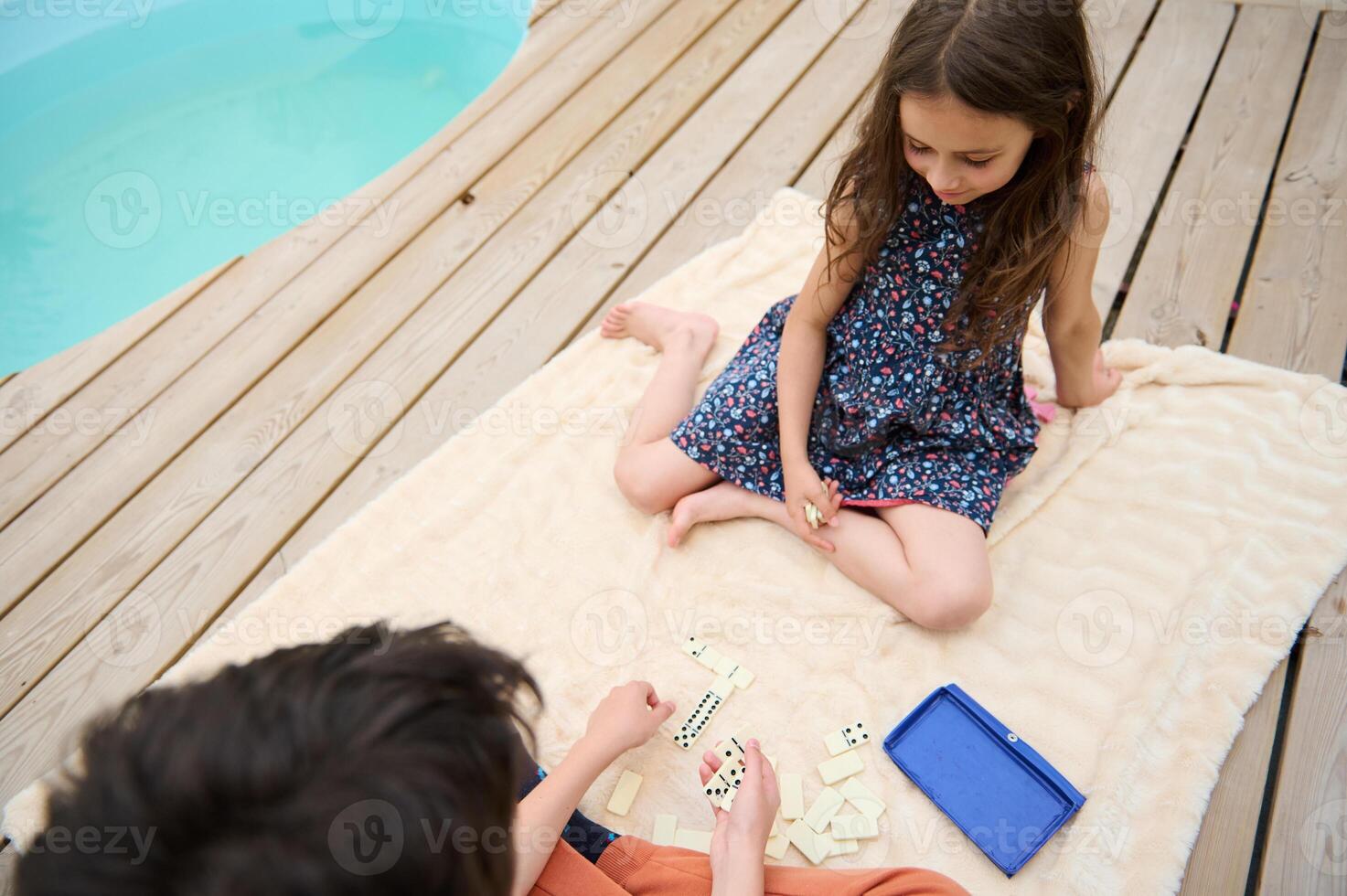 Children playing dominoes by the pool on a warm summer day, enjoying fun and relaxation outdoors with family and friends, showcasing playful moments and leisure activities. photo