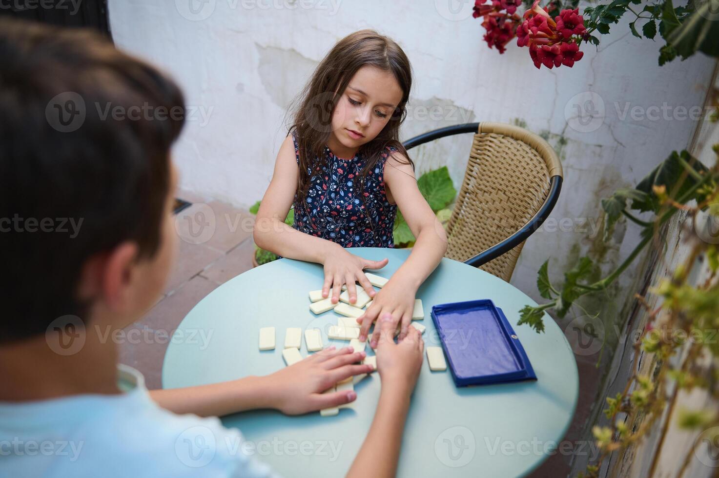 Children playing a board game together on a bright outdoor patio, enjoying a fun and engaging activity in a relaxed environment surrounded by lush plants and vibrant flowers. photo