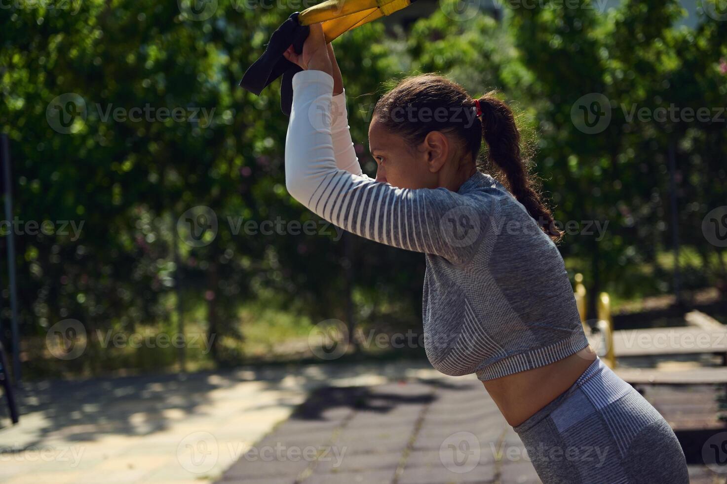 Young woman working out with resistance bands outdoors, enjoying fitness training in a park setting on a sunny day photo