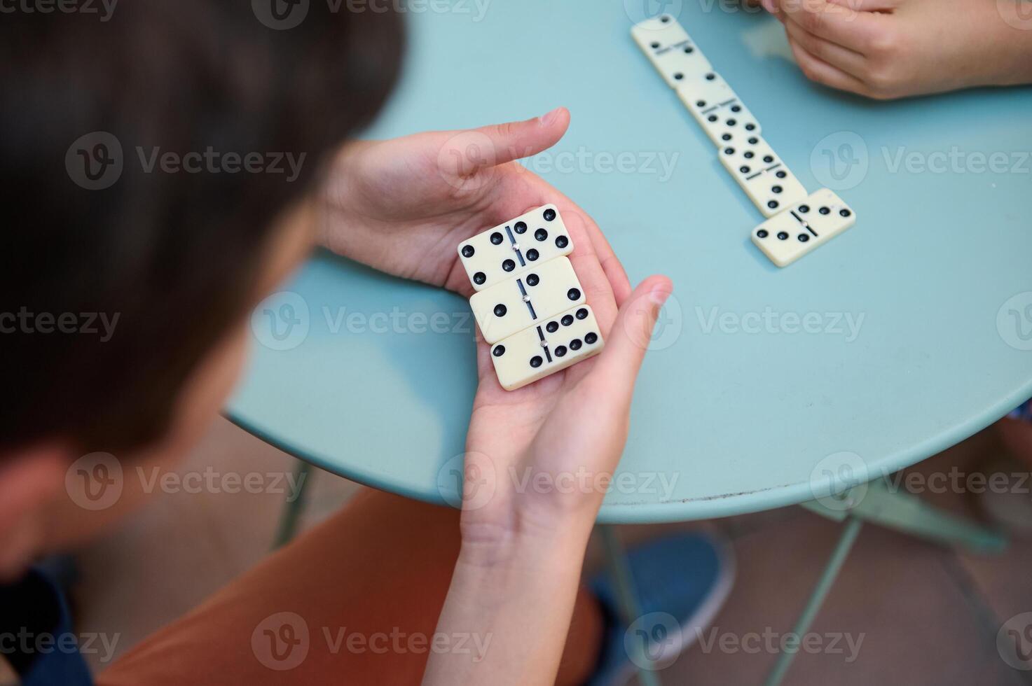Close-up of hands playing dominoes on a blue round table, showcasing a friendly board game interaction between friends or family in a relaxed and casual setting. photo