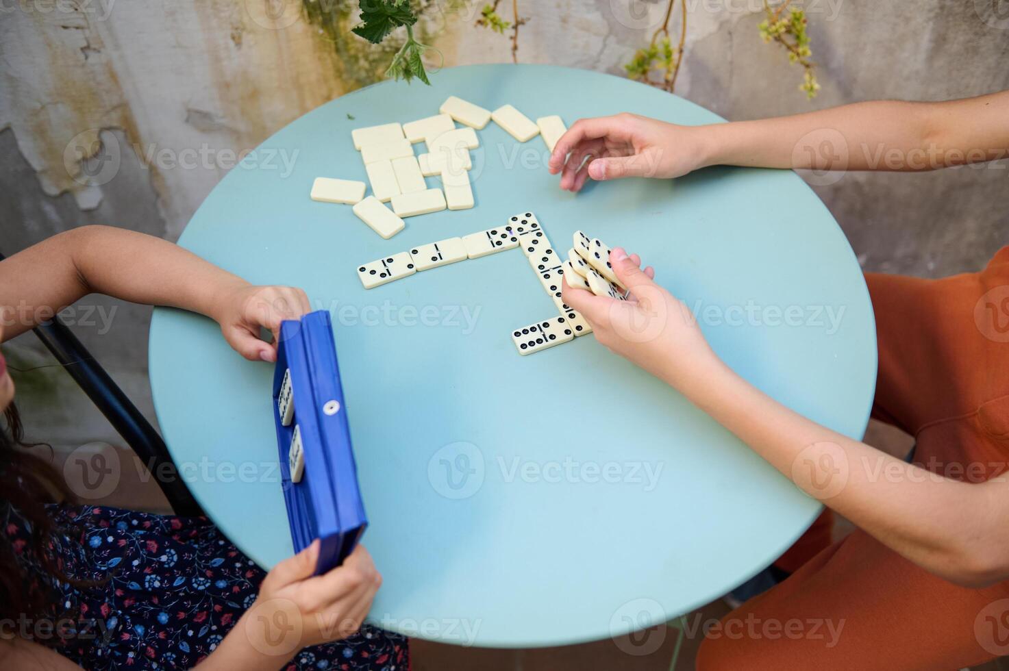 Children playing dominoes at a round blue table, focused on the game, enjoying quality time and developing strategy skills in a relaxed environment photo