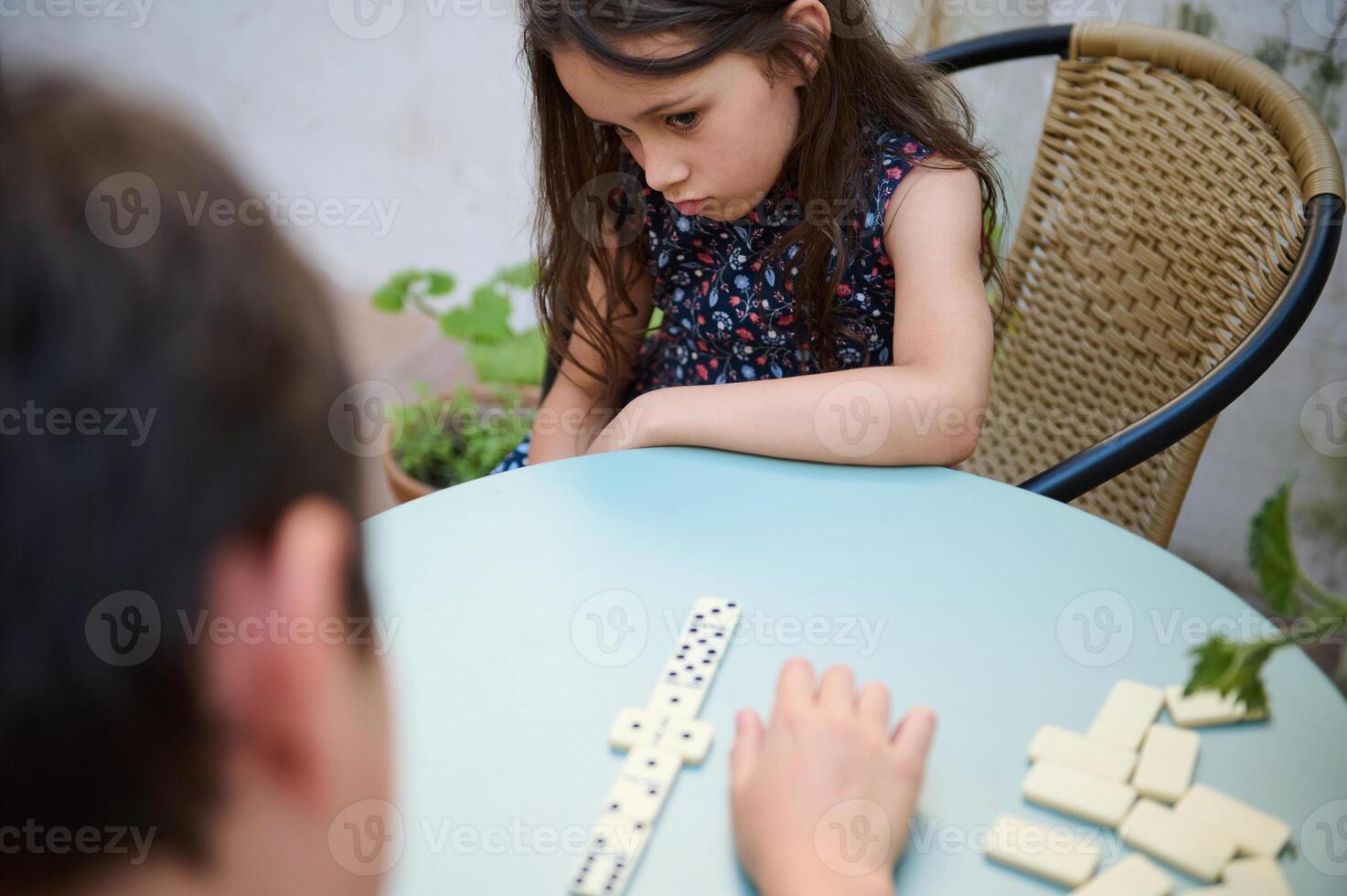 Thoughtful young girl playing a game of dominoes with a friend, captured in a moment of concentration at the table. photo
