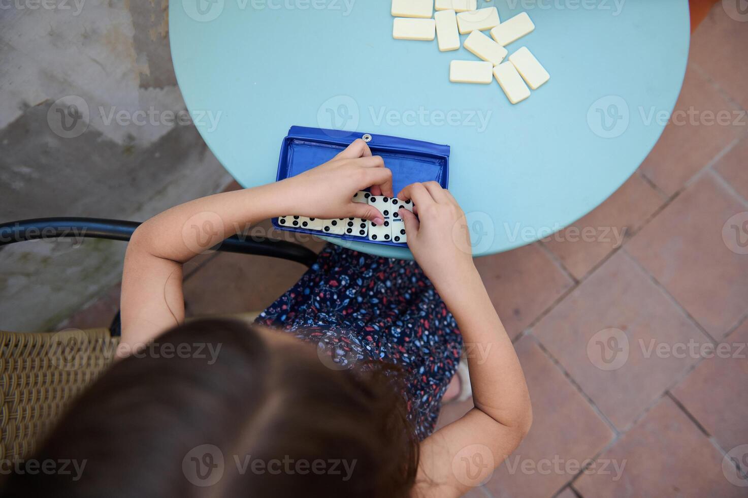 Young girl playing a game of dominoes on a patio, engaging in fun and learning while enjoying outdoor leisure time photo