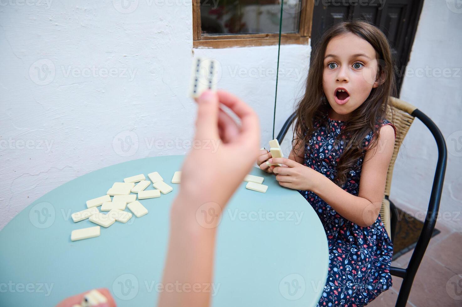Surprised young girl playing dominoes outdoors, showing excitement and emotion in a playful setting with a focus on strategy and fun. photo
