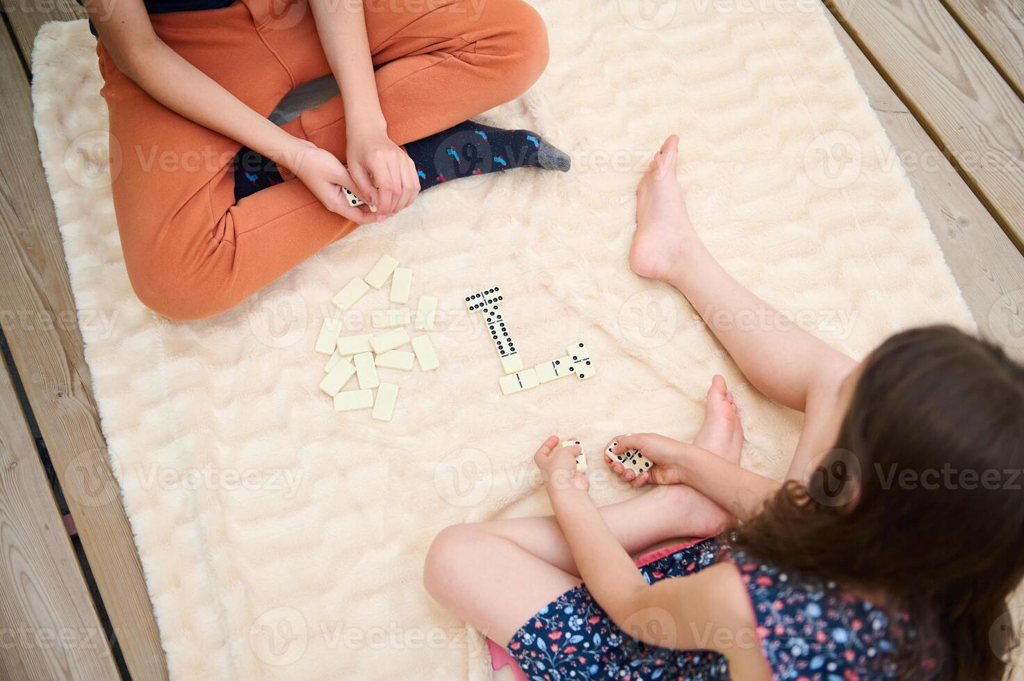 Children playing a fun game of dominoes on a soft beige blanket, enjoying a cozy indoor afternoon, connecting over a classic board game in a warm and comfortable setting photo