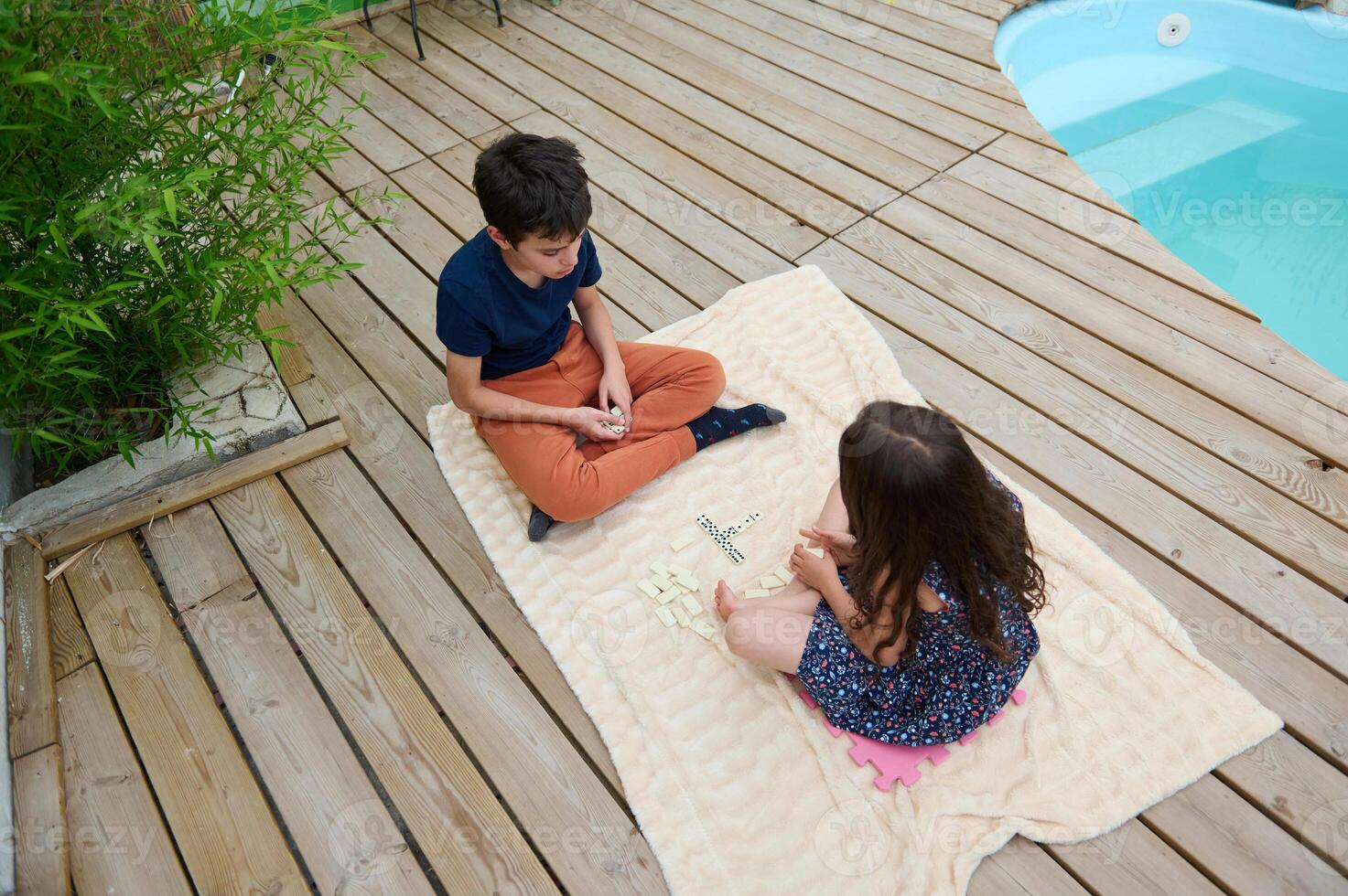 Children enjoying a fun game of word tiles on a cozy blanket by the poolside, creating a perfect summer day scene filled with laughter and creativity. photo