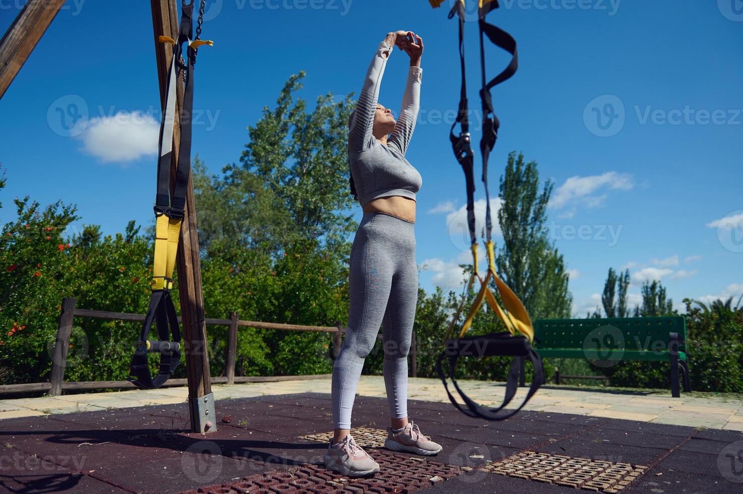 Woman exercising in an outdoor gym using suspension trainer for fitness and strength in a park under a clear blue sky. photo