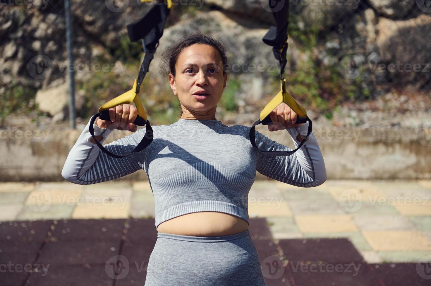 Woman exercising with TRX suspension trainer outdoors for fitness and strength training photo