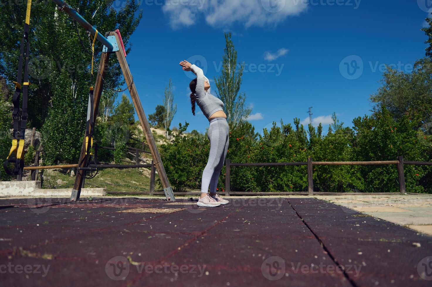 Woman stretching outdoors at a sunny fitness park, reaching towards the sky in a serene exercise routine. Capturing tranquility and focus in a natural environment for a healthy lifestyle. photo