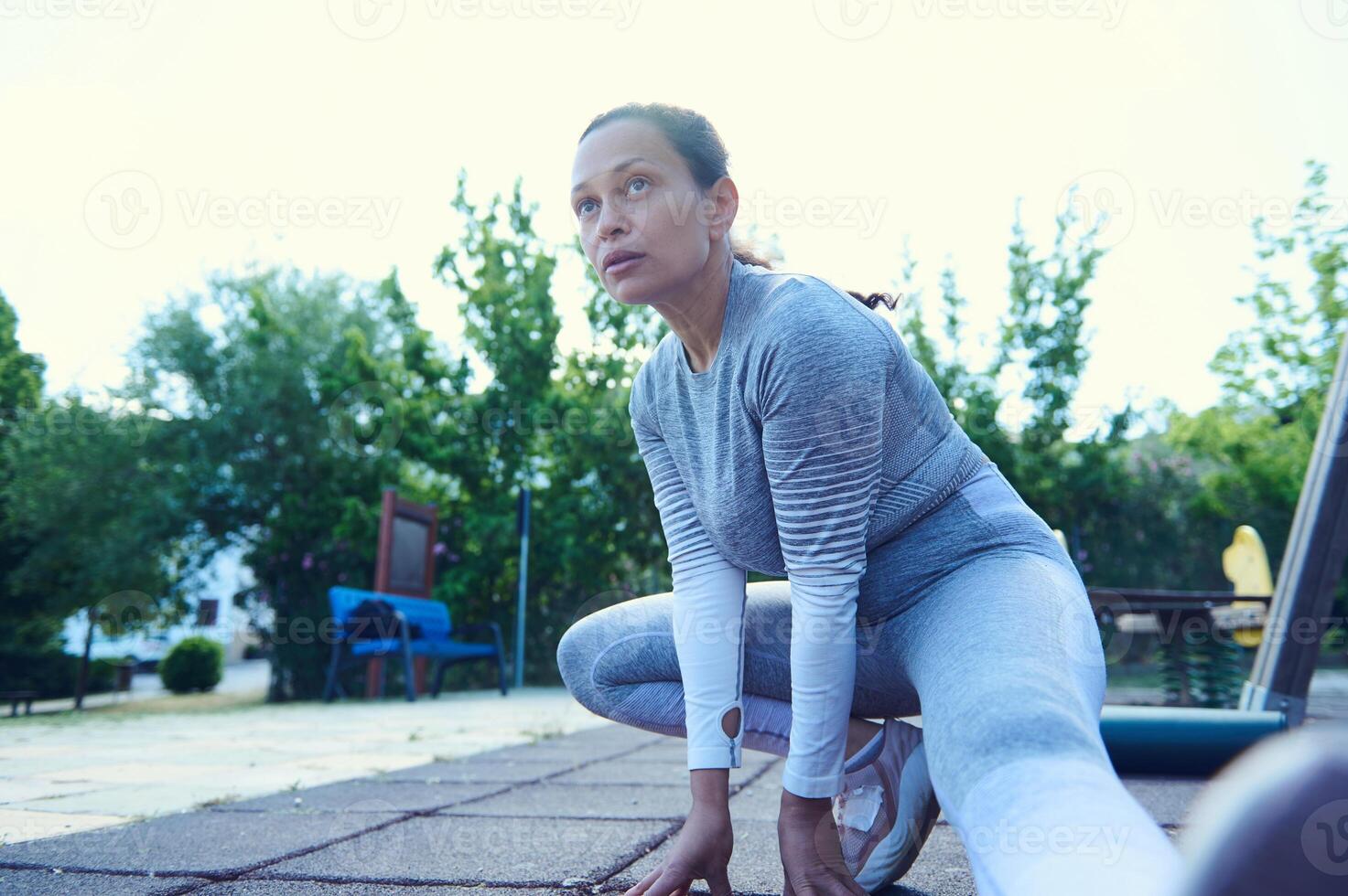 Woman in athletic attire warming up with a stretch outdoors on a sunny day, demonstrating focus, strength, and dedication to fitness in a green park setting photo