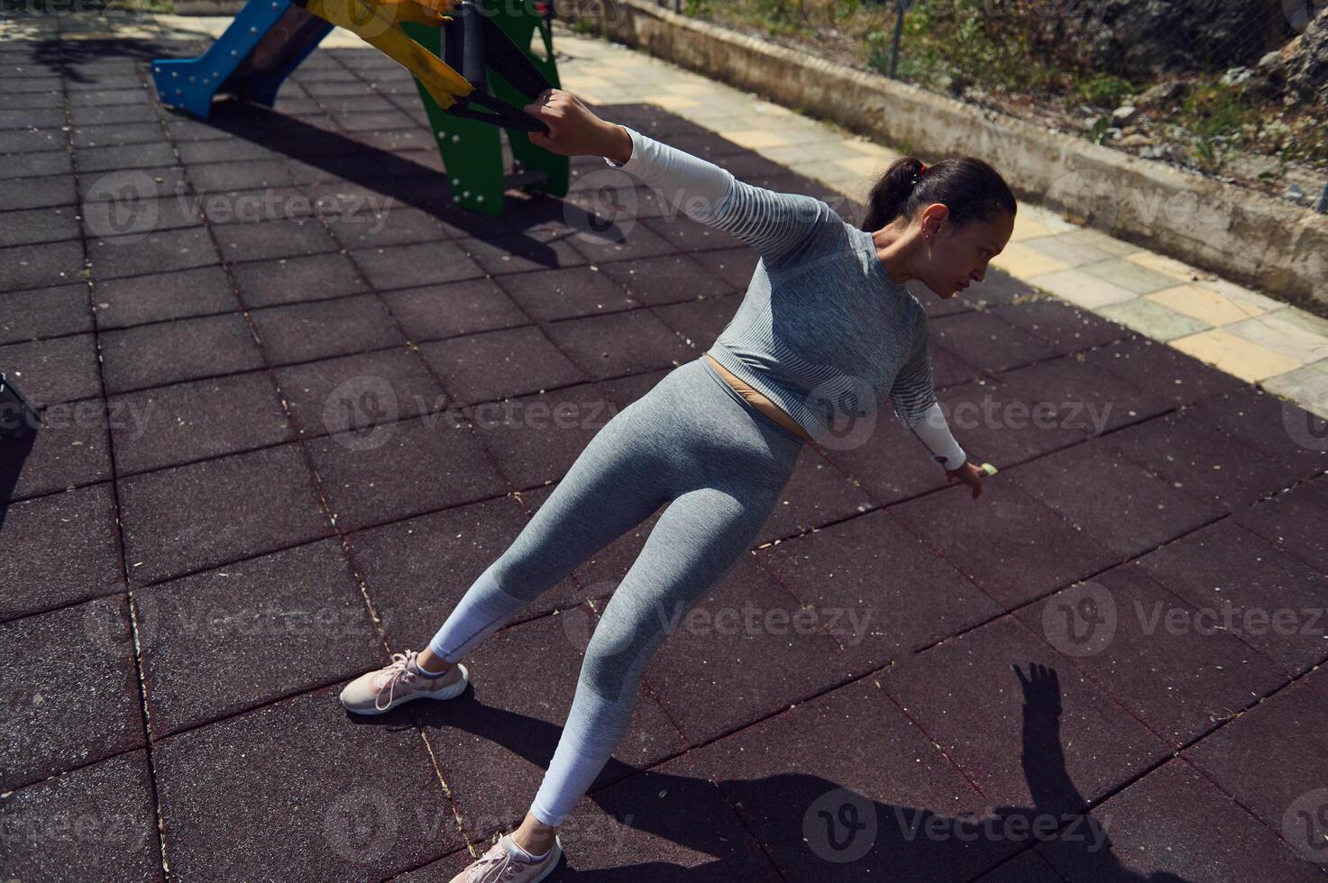 Active woman exercising outdoors in a sunny park, leaning back in a stretching pose on a textured surface, promoting fitness and healthy lifestyle in a relaxed, natural environment photo