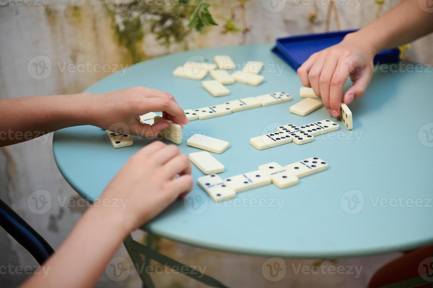 Close-up of hands playing a dominoes game on a blue table, focusing on strategy and creativity in a casual setting. Perfect for concepts of leisure, fun, and social interaction. photo