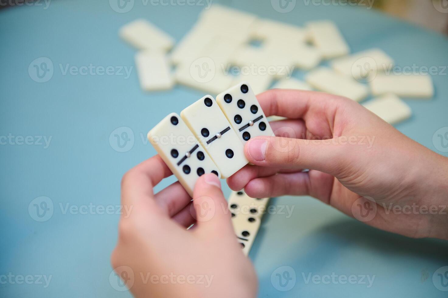 Hands holding white domino tiles during a strategic board game session on a blue table background photo