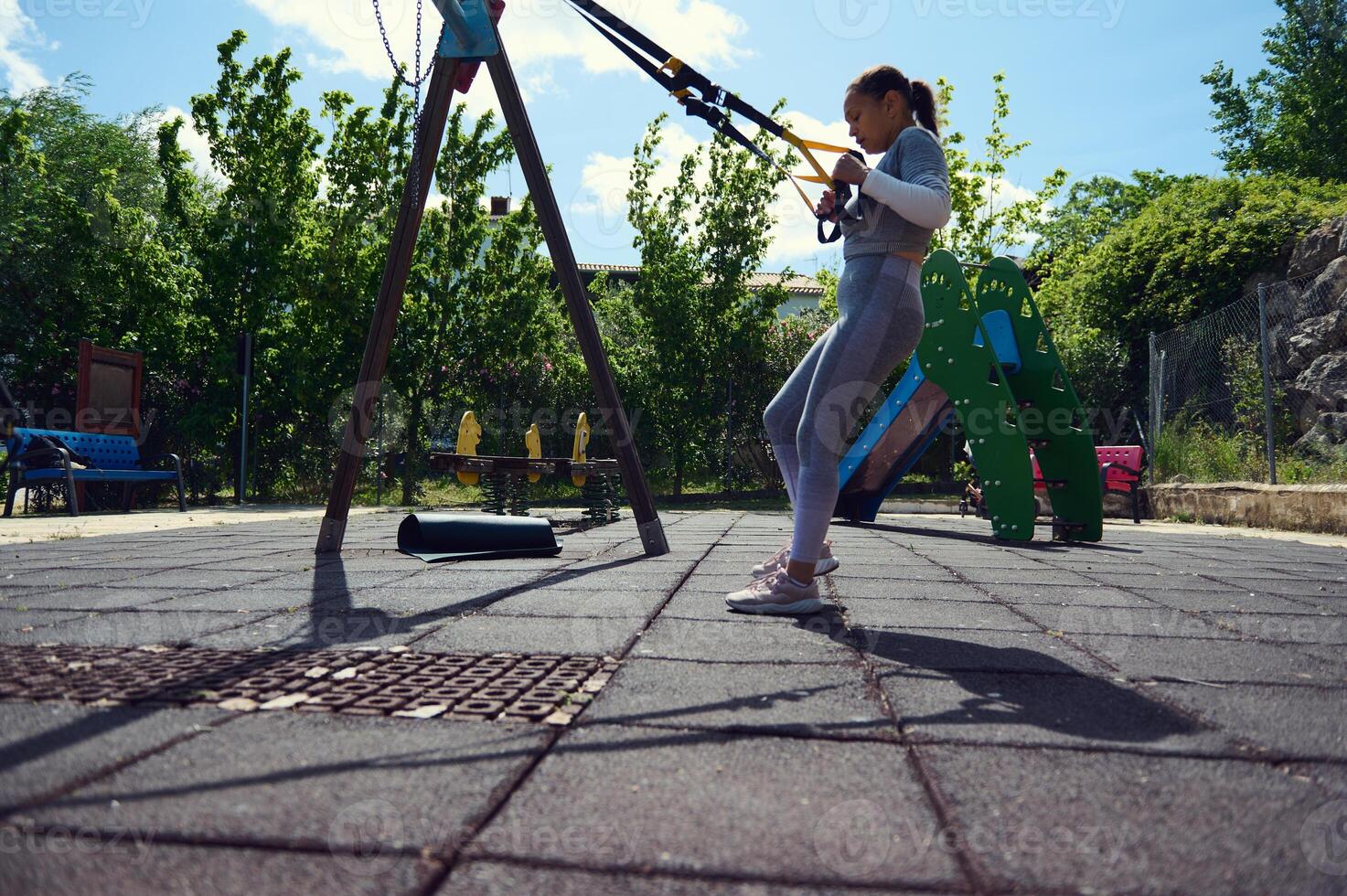 Woman exercising with resistance bands in an outdoor playground under a sunny sky, showcasing a healthy lifestyle and fitness dedication. photo
