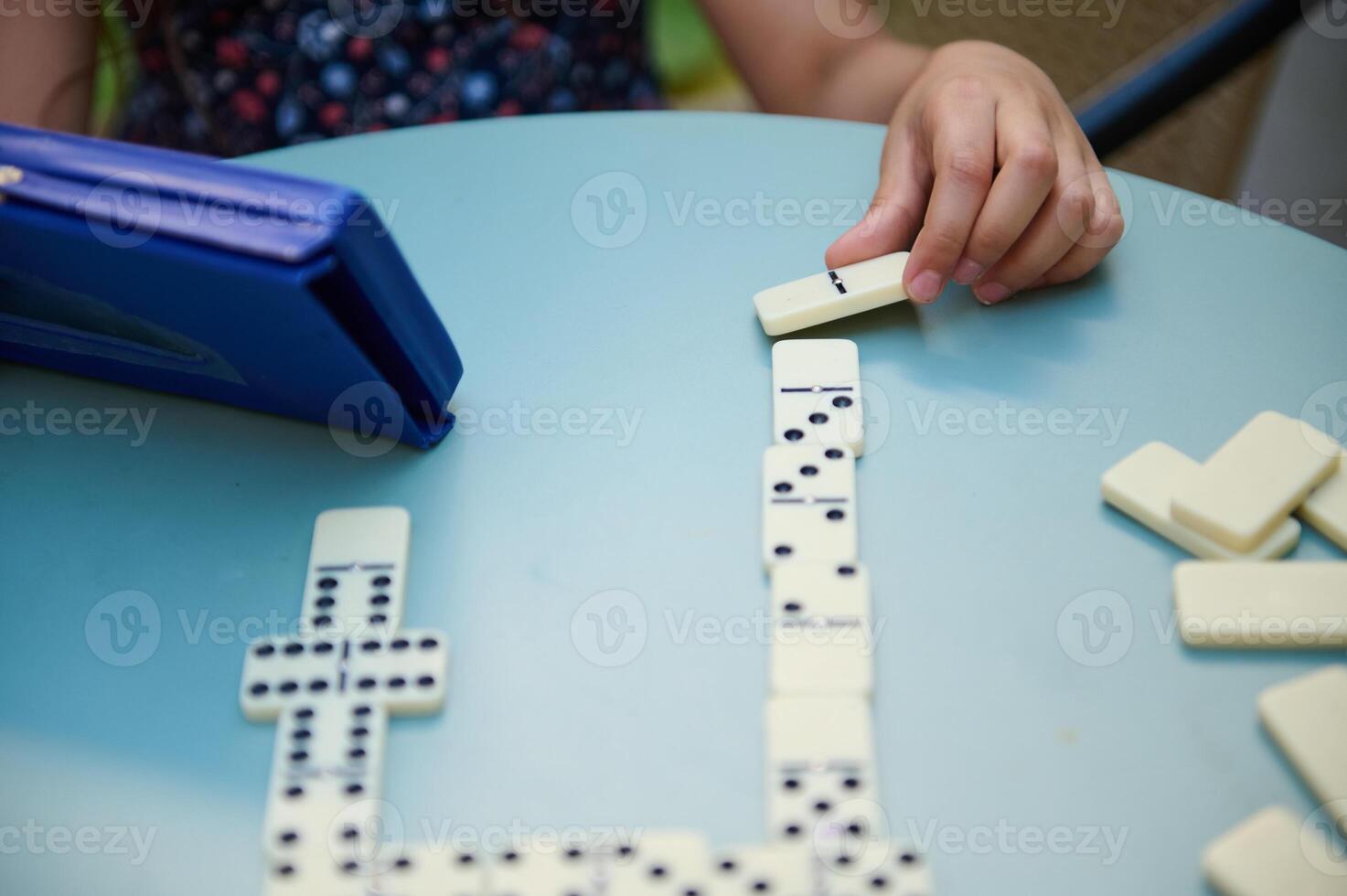 Child playing dominoes at a blue table, focusing on strategic moves and fun gameplay with a domino set. Kids engaging in classic board game. photo