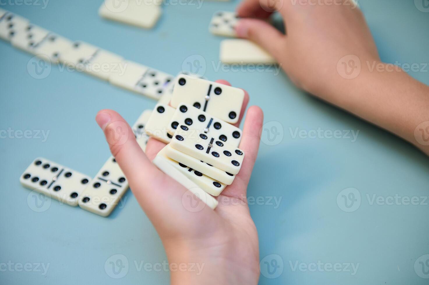 Hands playing dominoes on a light blue table express strategy, fun, and concentration in this engaging tabletop game setting. photo