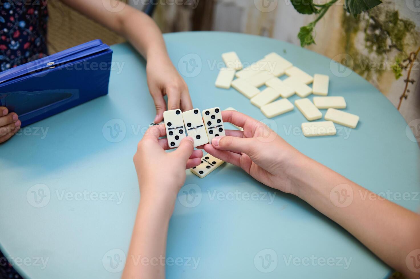 Children playing a game of dominoes at a round blue table, focusing on strategy and fun in a relaxed setting with friends. photo