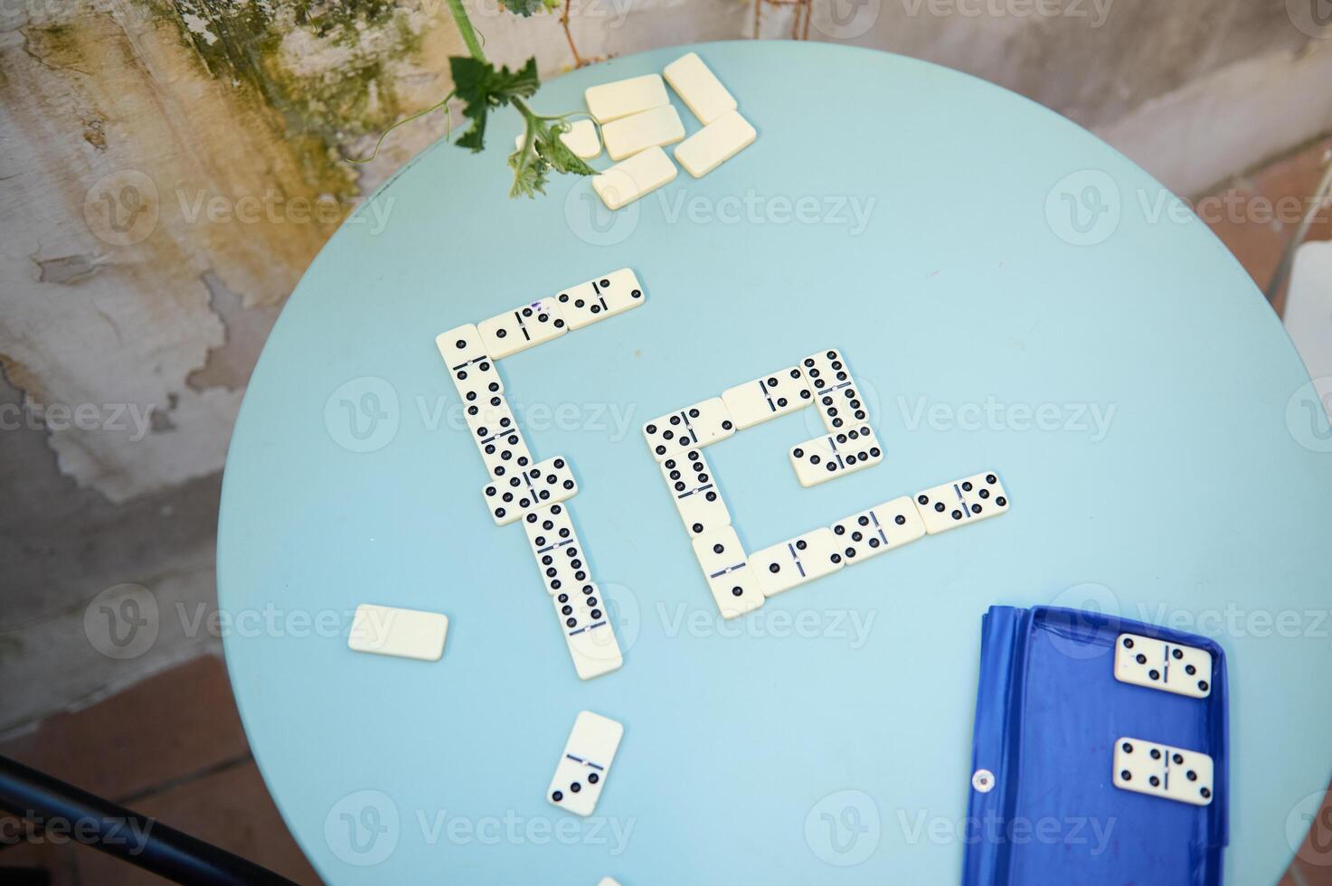 Dominoes arranged on a blue round table in an outdoor setting, showcasing strategy and leisure in a game setup with a vintage ambiance. photo