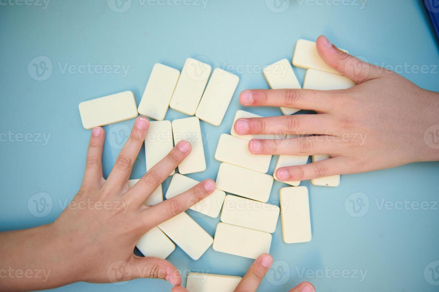 Children playing with white domino tiles on a blue table, showcasing teamwork and strategy in a fun and engaging way through hands-on learning and development. photo