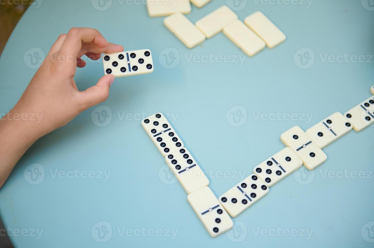 Close-up of a person's hand holding a domino piece while playing a game on a blue table, depicting strategy and leisure photo