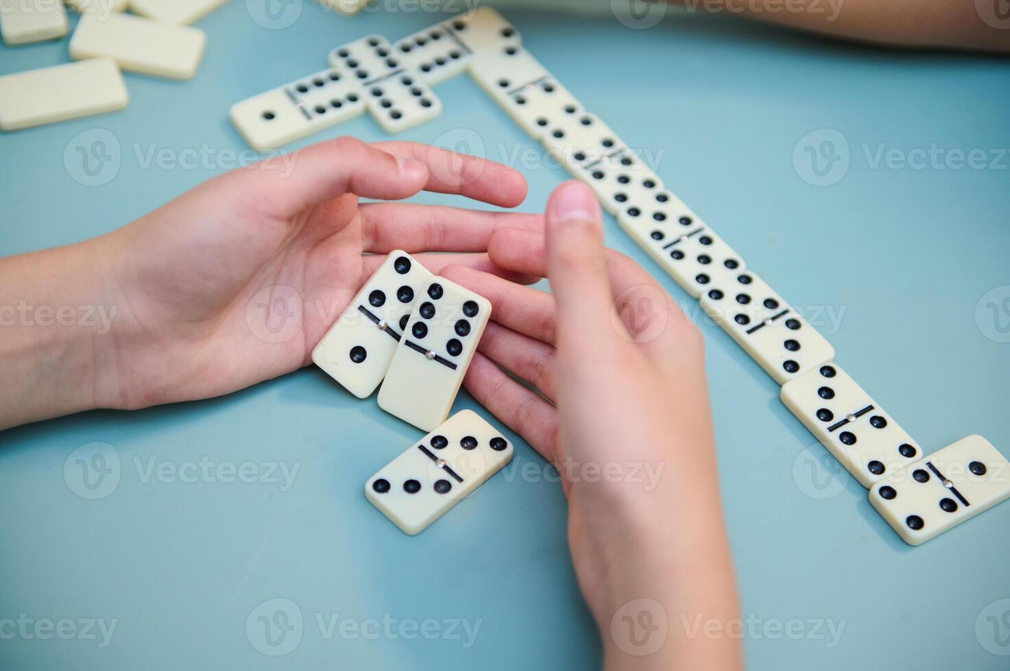 Hands playing a strategic game of dominoes on a light blue table, showcasing skill and focus during a fun and engaging board game session photo