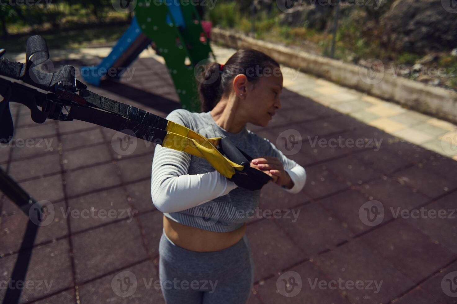 Woman exercising with TRX bands at outdoor gym in the park on a sunny day, focusing on strength and flexibility training photo
