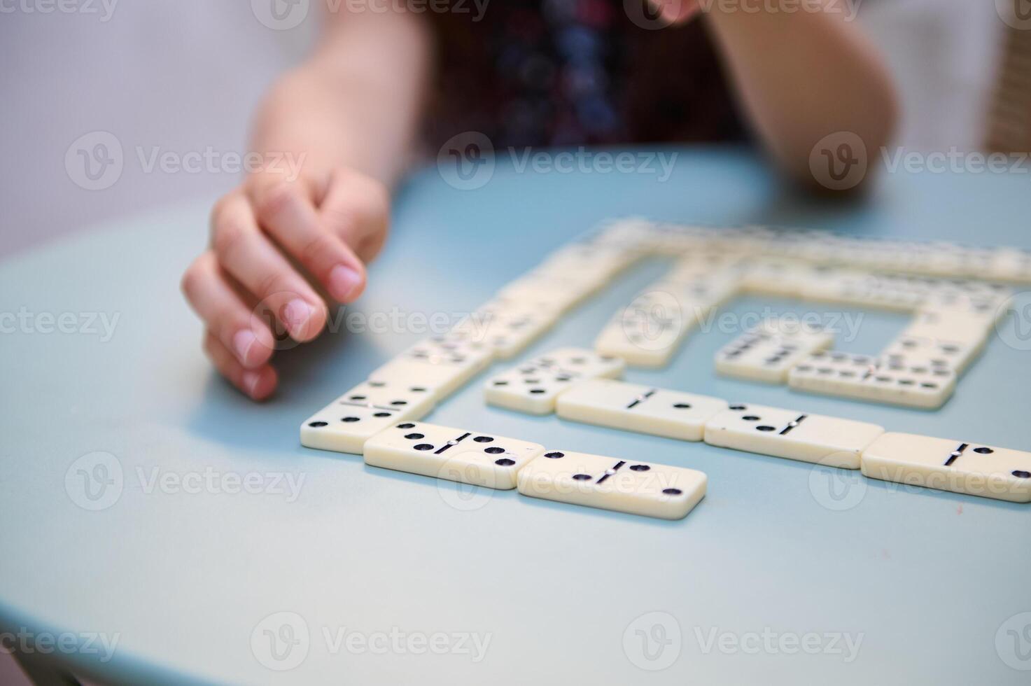 Close-up of a hand playing a strategic game of dominoes on a blue table, highlighting focus and concentration in strategic family board games. photo