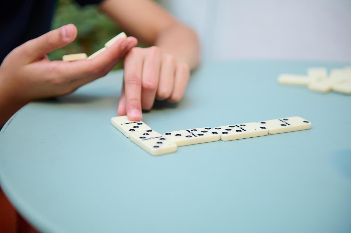 Hands engaged in a strategic game of dominoes on a pastel blue table, capturing concentration and enjoyment in a casual setting. photo