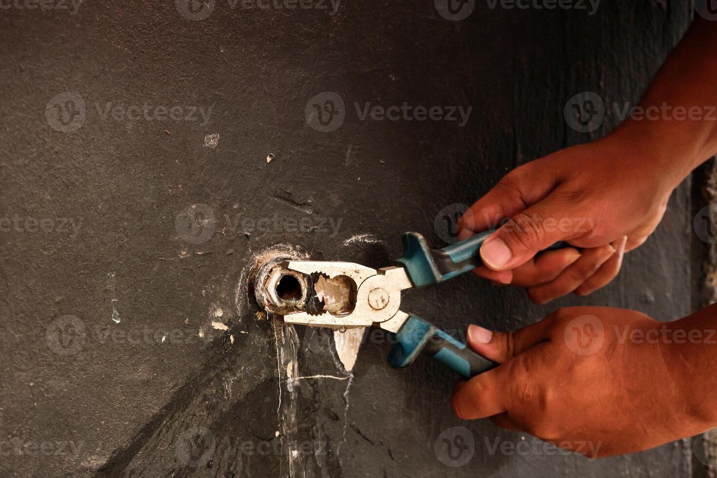 Hand of Asian Plumber Fixing Broken Water Tap on the Wall using Pliers photo