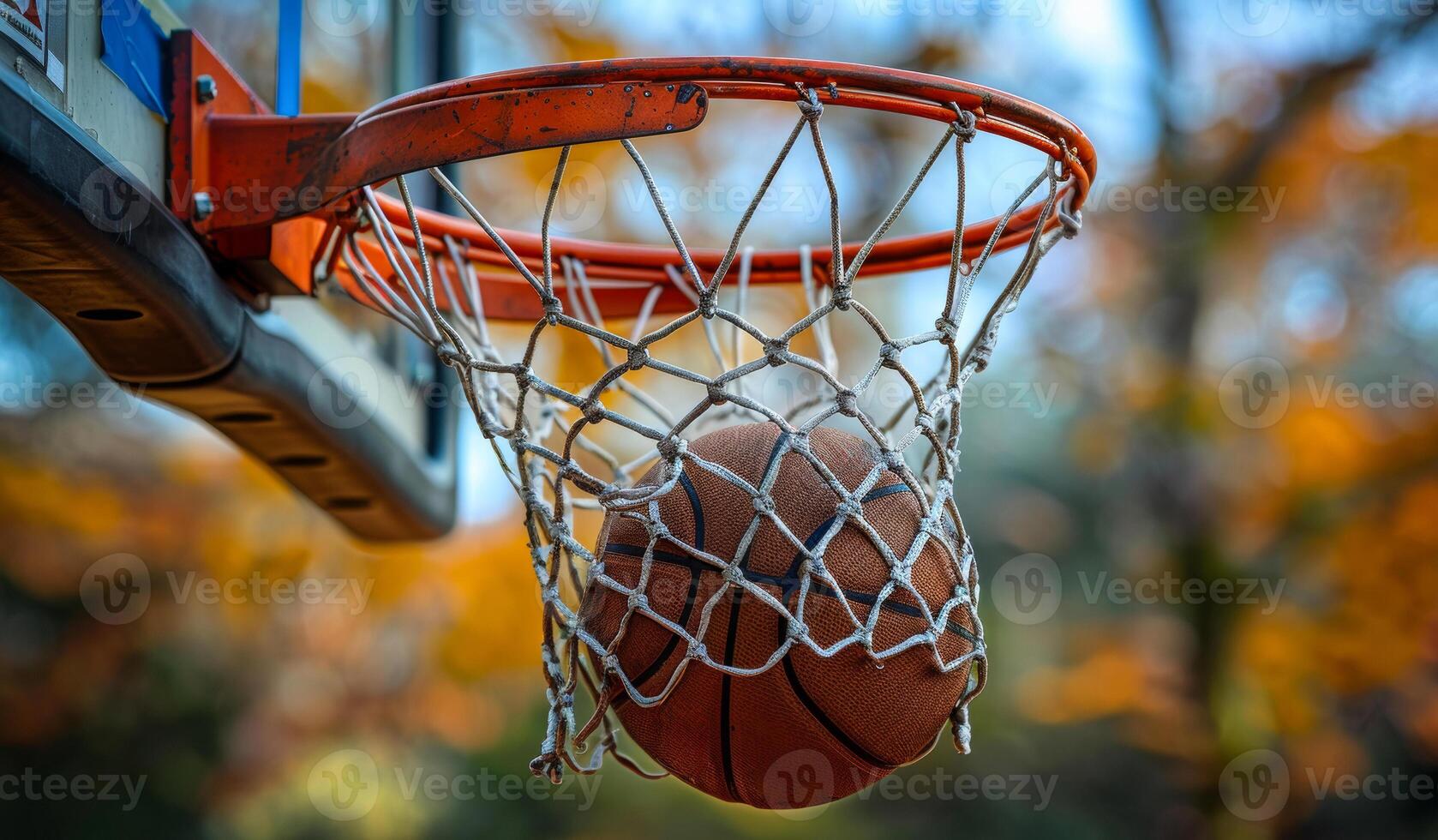 A basketball is in the net of a basketball hoop. The ball is brown and he is wet photo