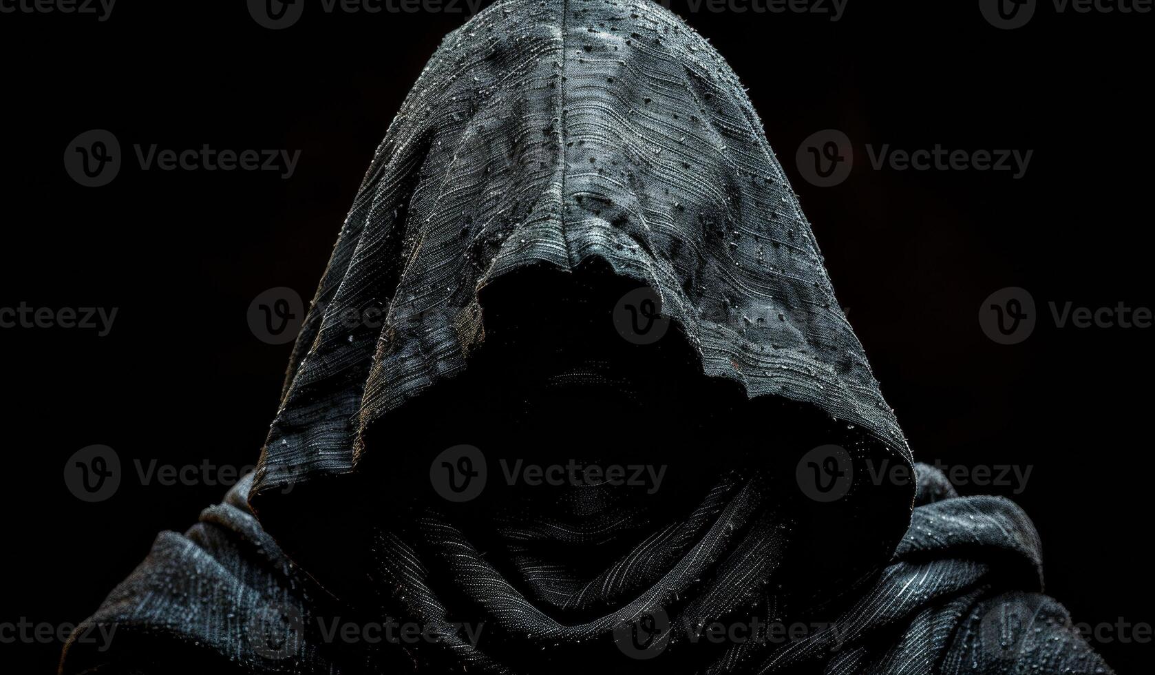 A hooded figure is shown in a dark room. The hood is pulled up, covering the face and creating a sense of mystery and darkness. The image evokes a mood of suspense and intrigue photo