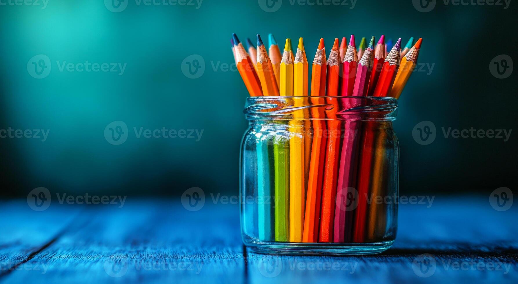 A jar full of colorful pencils on a wooden table. The pencils are arranged in a rainbow pattern, with the colors ranging from red to yellow to green. The jar is placed on a blue surface photo