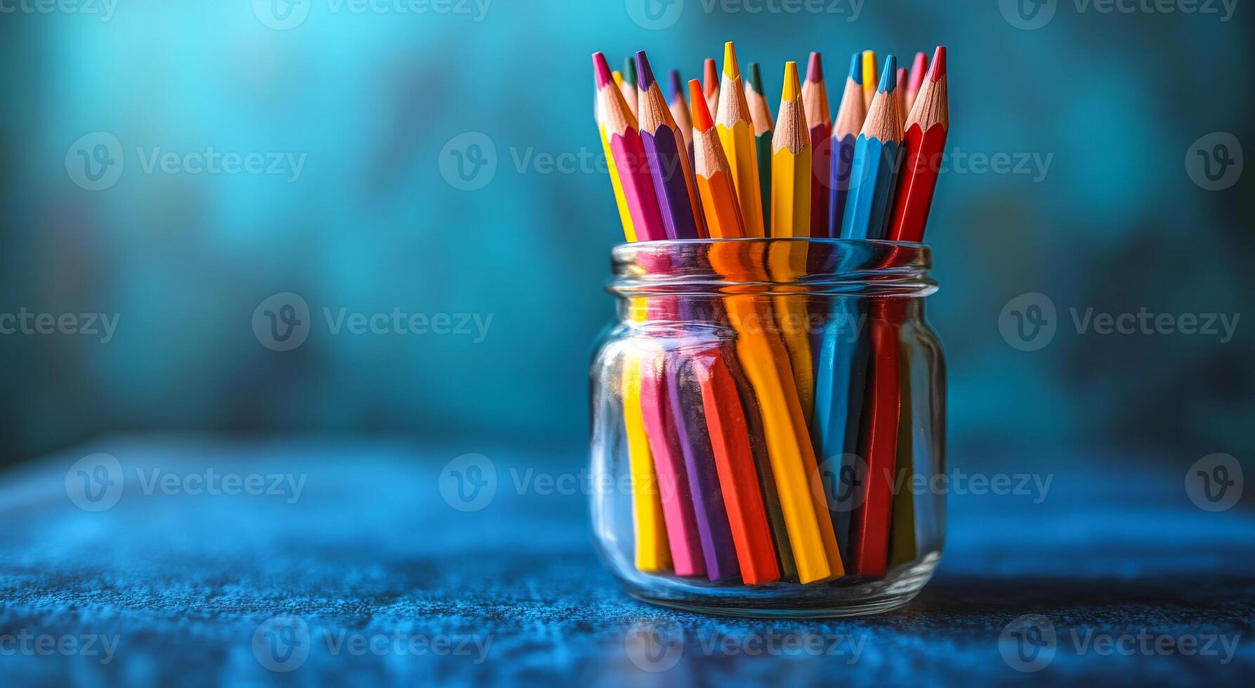 A jar full of colored pencils on a blue table. The pencils are in different colors and are arranged in a way that they are all visible photo