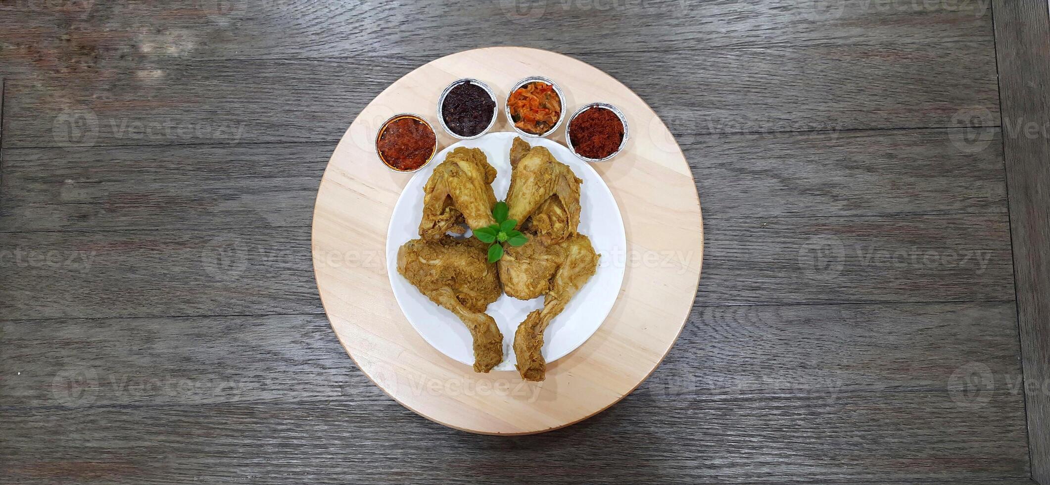 Ayam ungkep bumbu kuning or boiled chicken with curry seasoning and coconut water. Served with varian sambal or hot chili sauce. Ready to fried photo