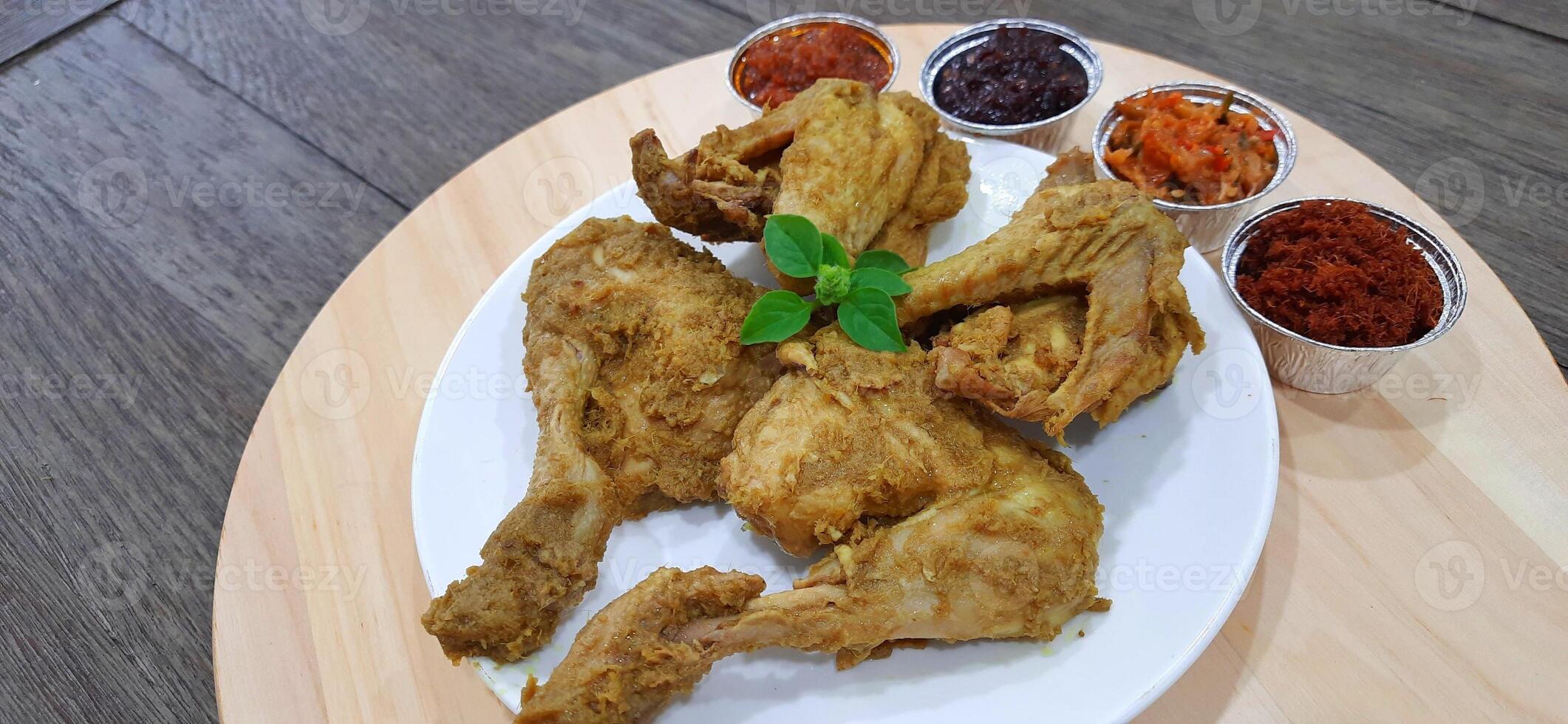 Ayam ungkep bumbu kuning or boiled chicken with curry seasoning and coconut water. Served with varian sambal or hot chili sauce. Ready to fried photo