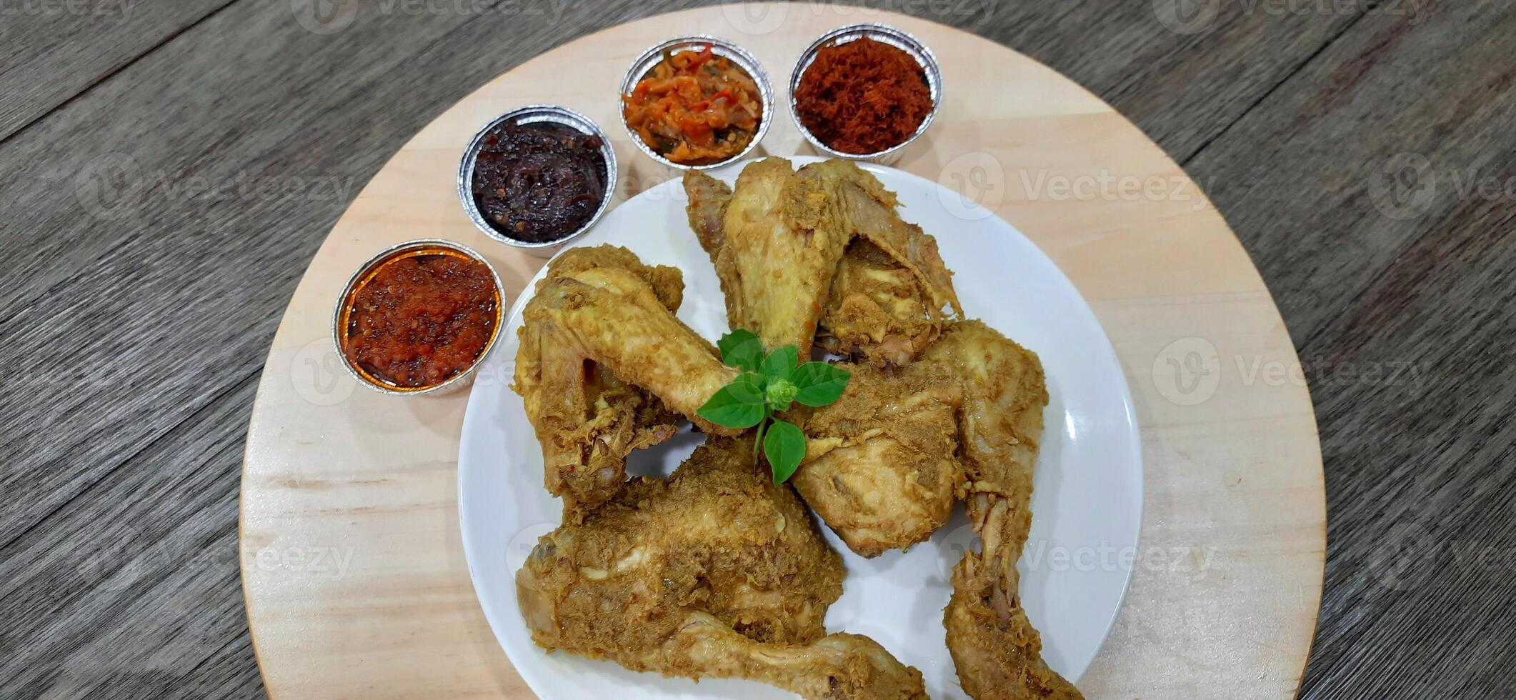 Ayam ungkep bumbu kuning or boiled chicken with curry seasoning and coconut water. Served with varian sambal or hot chili sauce. Ready to fried photo